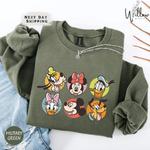 A green sweatshirt with a graphic of Disney characters, including Goofy, Minnie Mouse, Donald Duck, Mickey Mouse, Donald Duck's ducklings, and Pluto, arranged in a circular pattern.
