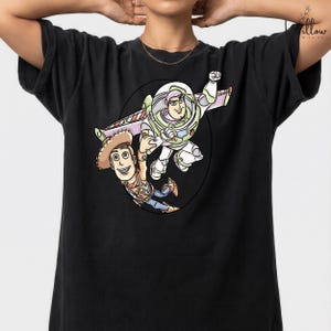 A black t-shirt with a graphic design featuring two cartoon characters from the Toy Story franchise - Buzz Lightyear and Woody.
