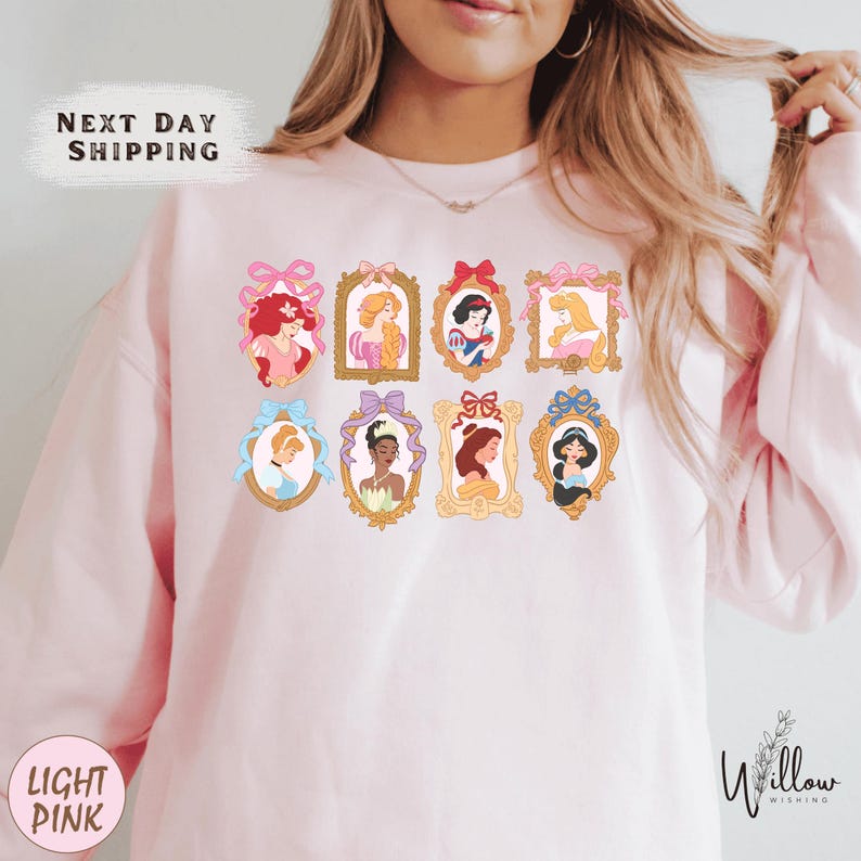 A woman wearing a pink sweatshirt with a graphic of Disney princesses on it.
