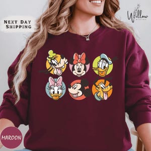 A woman wearing a burgundy sweater with a graphic of Disney characters on it.