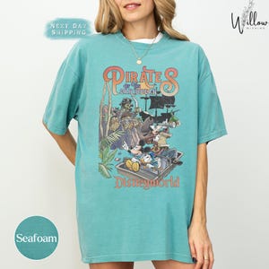 A woman wearing a turquoise t-shirt with a graphic of Disney's Pirates of the Caribbean on it.