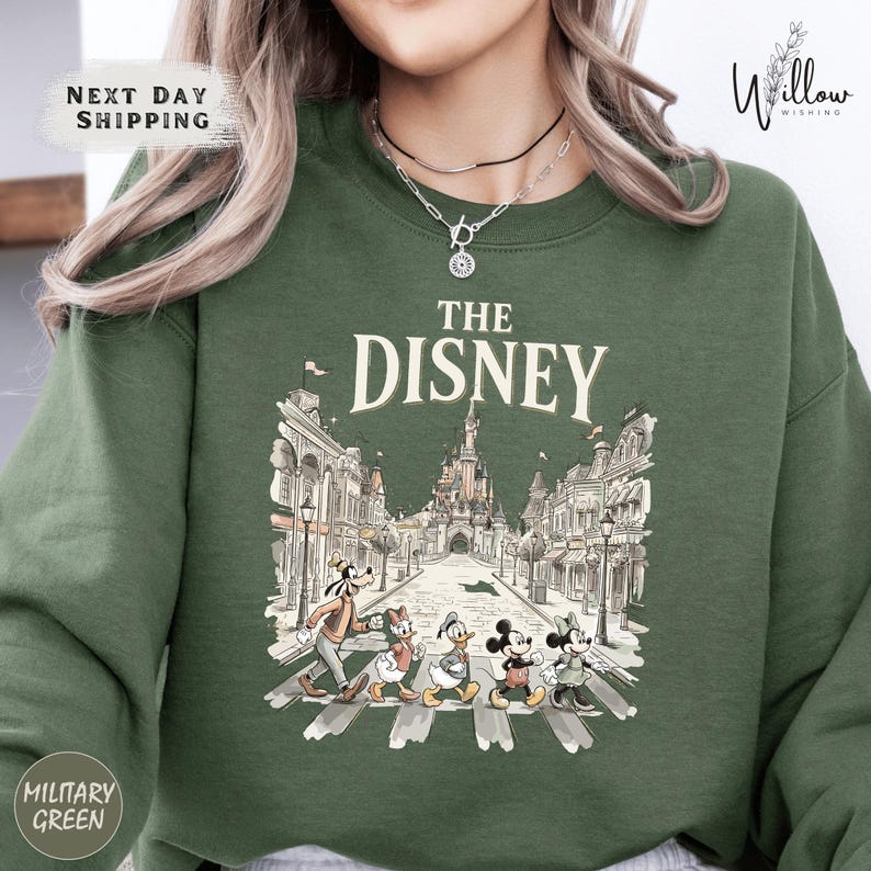 A woman wearing a green sweatshirt with a graphic of Disney characters crossing the street.