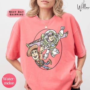 A woman wearing a pink t-shirt with a graphic of a character from the Toy Story franchise, specifically Buzz Lightyear and Woody, depicted in a playful pose.