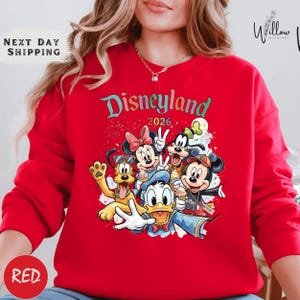 A woman wearing a red sweater with a Disney-themed graphic of Minnie Mouse, Donald Duck, Mickey Mouse, and Goofy.