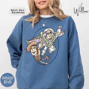 A woman wearing a blue sweatshirt with a cartoon image of Buzz Lightyear and Woody from Toy Story printed on it.