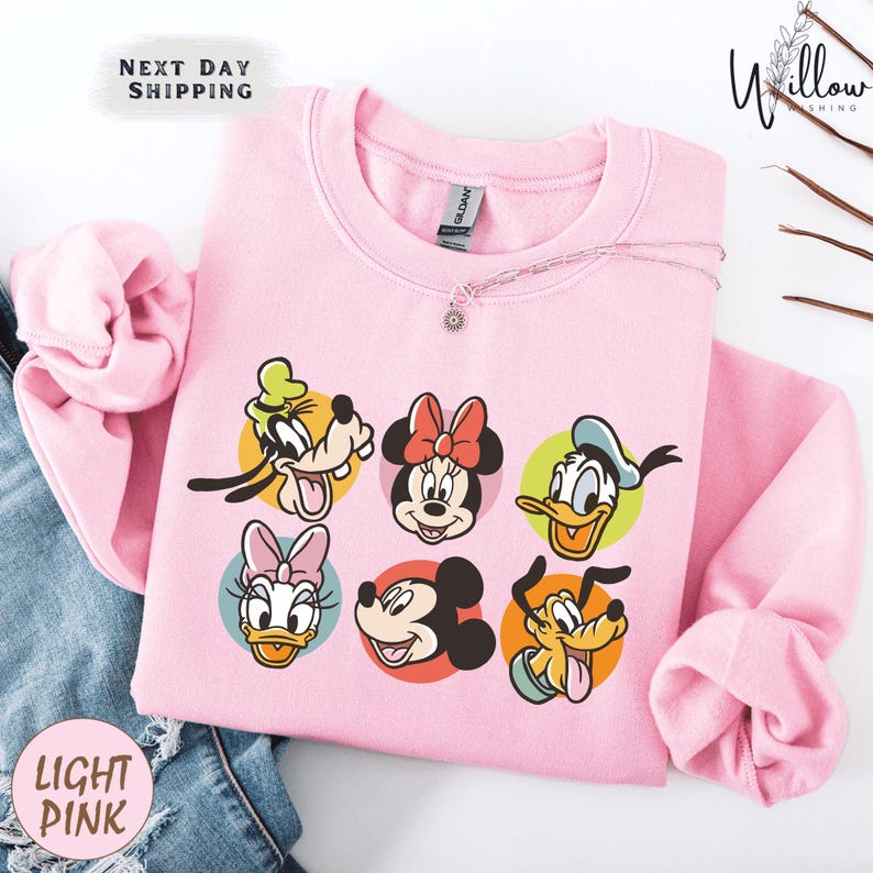 A pink sweatshirt with a cartoon character design, featuring Minnie Mouse, Goofy, Mickey Mouse, Donald Duck, Donald Duck's ducklings, and Pluto.
