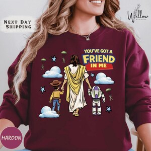 A woman wearing a maroon sweater with a graphic design depicting a cartoon-style illustration of Jesus Christ holding a child and a robot.