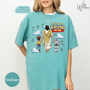 A woman wearing a teal t-shirt with a graphic design depicting a cartoon depiction of Jesus Christ and two children.