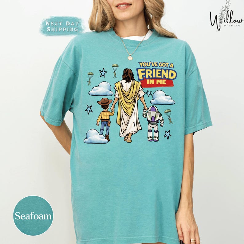 A woman wearing a teal t-shirt with a graphic design depicting a cartoon depiction of Jesus Christ and two children.