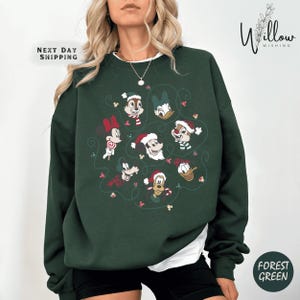 May include: Forest green sweatshirt featuring a festive design with Disney characters wearing Santa hats. The design includes Mickey, Minnie, Donald, Daisy, Goofy, and Chip and Dale. The text "Next Day Shipping" and "Willow Wishing" are also visible.