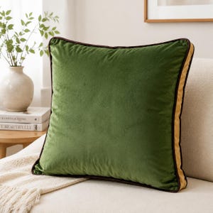 May include: A square throw pillow featuring a solid dark green velvet front panel, a contrasting mustard yellow side panel, and dark brown piping along the edges. The pillow has a soft, plush texture and a clean, structured square shape.