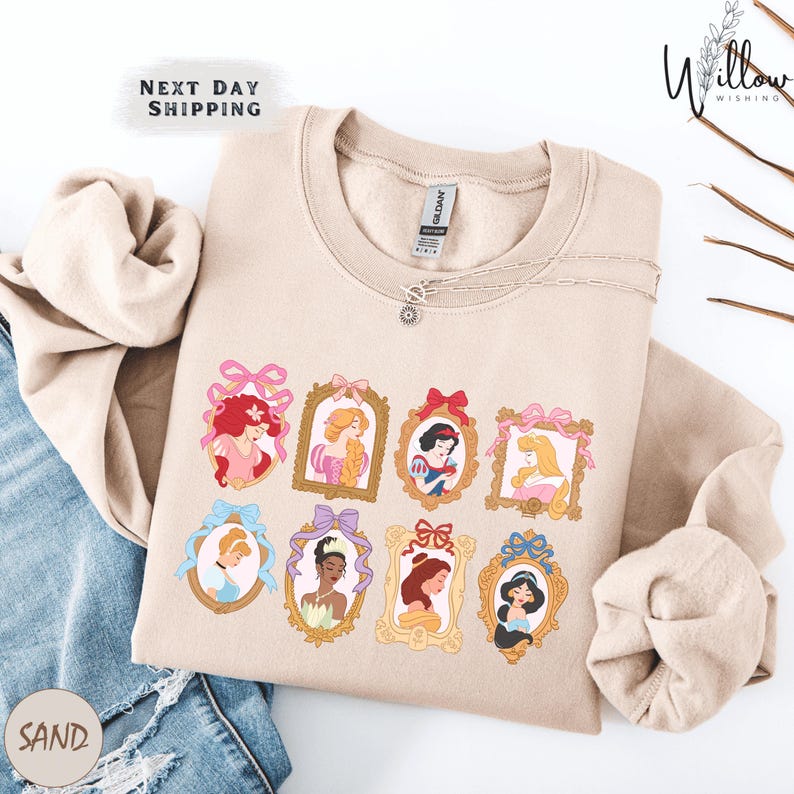 A beige sweatshirt with a graphic design featuring illustrations of various Disney princesses, including Snow White, Rapunzel, and other popular characters.
