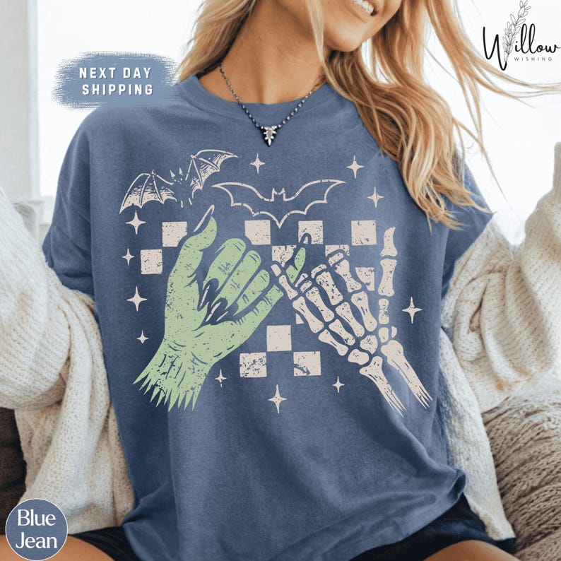 A woman wearing a blue t-shirt with a graphic design featuring a skeleton hand and bat-like symbols, along with the text "Next day shipping".