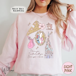 May include: Light pink sweatshirt with a graphic featuring a gold crown, owl, castle, and a framed image of a couple. The text "I know you... I walked with you. Once upon a dream" is printed on the front.