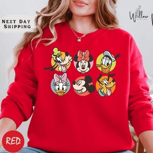 A woman wearing a red sweater with a graphic of Disney characters on it.