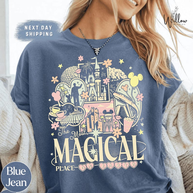 A woman wearing a blue t-shirt with a colorful graphic design featuring various Disney-themed elements such as Mickey Mouse, Eiffel Tower, and other iconic landmarks.