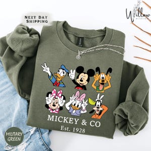 A green sweatshirt with a graphic of Disney characters Mickey Mouse and Donald Duck, along with the text "MICKEY & CO Est. 1928".
