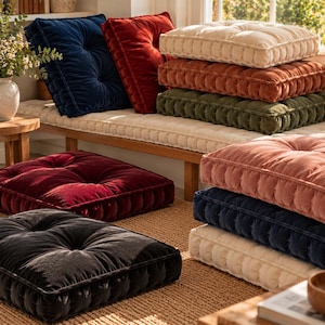 May include: A collection of square velvet floor cushions in various colors including navy blue, deep red, cream, rust orange, olive green, and black. Each cushion features a tufted center, piped edges, and a thick, plush construction.