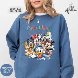 A woman wearing a blue sweatshirt with a colorful graphic of Disney characters from the theme park.