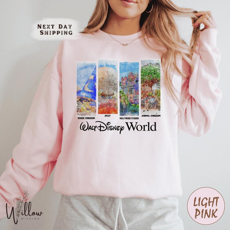 A woman wearing a pink sweatshirt with a collage of Disney World images on it.