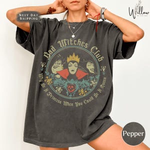 A person wearing a gray t-shirt with a graphic design featuring characters from the Disney film "Bad Witches".