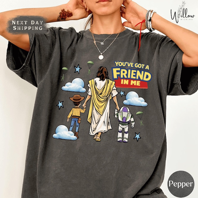 A person wearing a gray t-shirt with a graphic design depicting a religious figure, a boy, and a robot, along with the text "You've got a FRIEND in me".