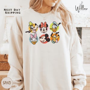 A person wearing a white sweatshirt with a graphic of six cartoon character faces arranged in a row.