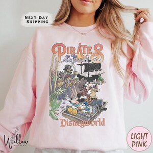 A woman wearing a pink sweatshirt with a graphic of Disney characters from the Pirates of the Caribbean franchise.