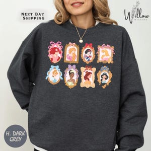 A woman wearing a gray sweatshirt with a graphic design of various Disney princesses in frames.