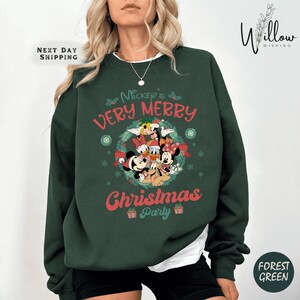 May include: Forest green sweatshirt featuring Mickey Mouse and friends. The design includes the text "Mickey's Very Merry Christmas Party" in red and white. The sweatshirt has a crew neck and long sleeves.