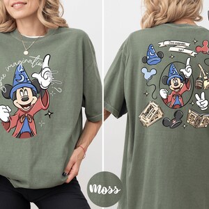 A woman wearing a green t-shirt with a graphic of Mickey Mouse and various Disney-themed elements.