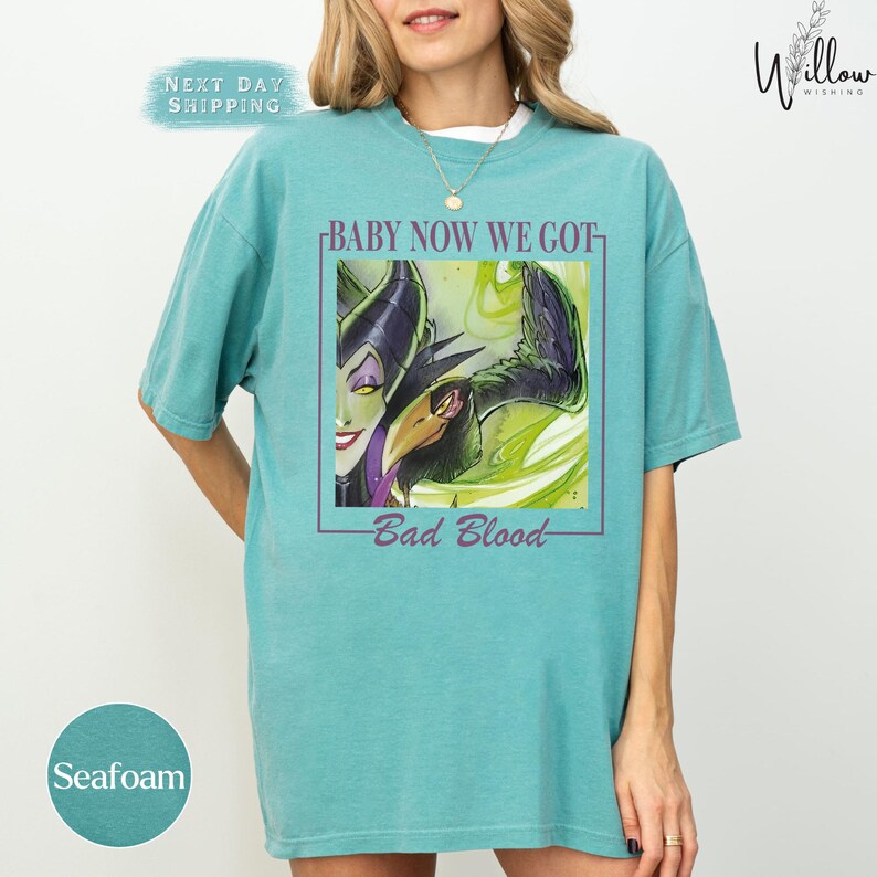 A woman wearing a teal t-shirt with a graphic design featuring a character from the Disney movie "Bad Blood".