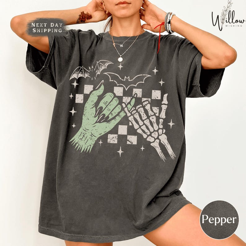 A person wearing a black t-shirt with a graphic design featuring a skeleton hand and bat wings, along with a checkerboard pattern.