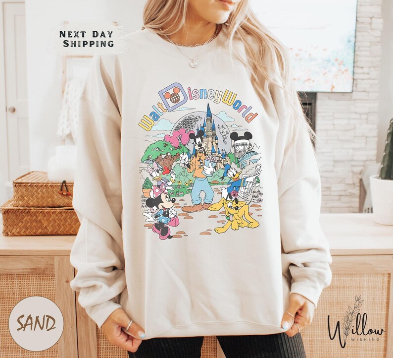 A woman wearing a white sweatshirt with a colorful graphic of Disney characters and landmarks, including Mickey Mouse and the castle of Disneyland.