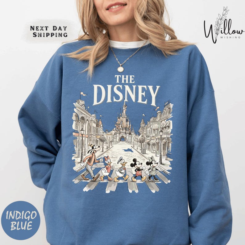 A woman wearing a blue sweatshirt with a graphic of Disney characters crossing the street.
