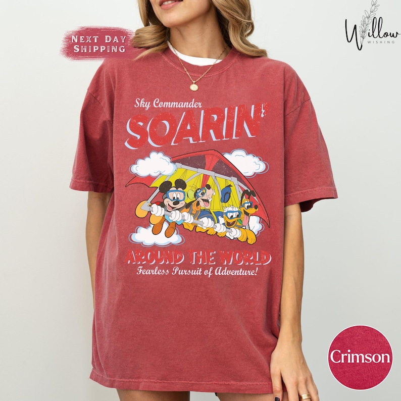 A woman wearing a red t-shirt with a cartoon image of Mickey Mouse and other characters, along with the text "Sky Commander SOARIN Around the World Fearless Pursuit of Adventure!" printed on it.