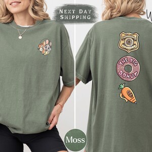 A woman wearing a green t-shirt with various cartoon characters and designs, including a police badge, a donut, and a carrot.