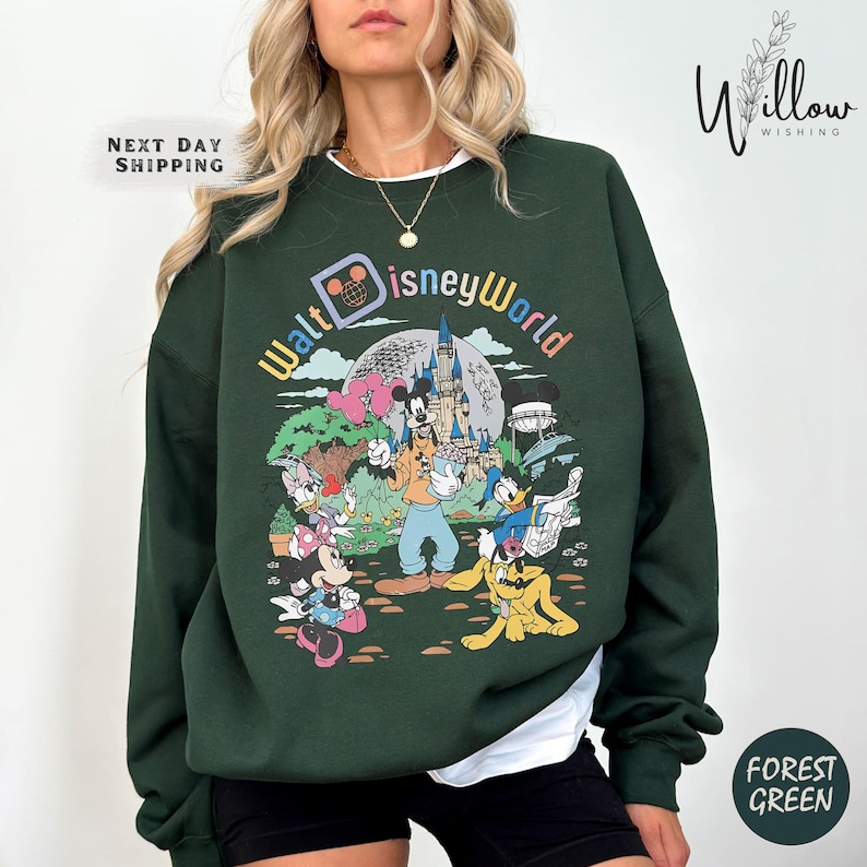 A woman wearing a green sweatshirt with a colorful graphic of Disney characters and landmarks.