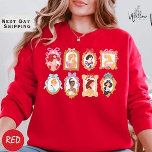 A woman wearing a red sweater with a collage of illustrations of Disney princesses on it.