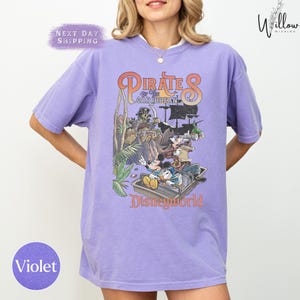 A woman wearing a purple t-shirt with a graphic design of Disney characters from the Pirates of the Caribbean ride at Disneyworld.
