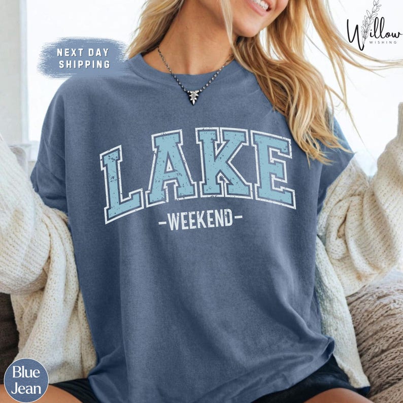 A woman wearing a blue t-shirt with the text "LAKEWEEKEND" printed on it, sitting on a couch.