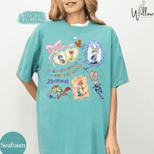 A woman wearing a teal t-shirt with various cartoon animal characters and designs printed on it.