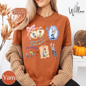 A woman wearing a brown t-shirt with various cartoon characters and designs, including a rabbit, a cat, and other animals. She is also wearing a necklace and has her hair blowing in the wind.