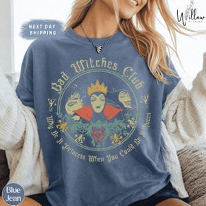 A woman wearing a blue t-shirt with a graphic design featuring characters from the Disney film "Bad Witches".