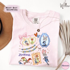 a pink t-shirt with various cartoon animal characters, including a rabbit, fox, and duck, along with other colorful illustrations. The t-shirt is displayed on a white background, and there is a hat and some decorative elements in the background.