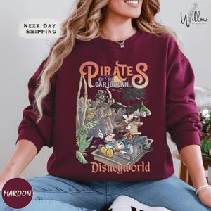 A woman wearing a burgundy sweatshirt with a graphic of Disney's Pirates of the Caribbean on it.