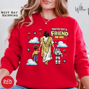 A red sweater with a cartoon illustration of a person holding a robot and a child, along with the text "You've got a Friend in Me" and a Bible verse reference.
