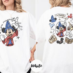 A white t-shirt with a graphic of Mickey Mouse and various Disney-themed elements, including a wizard hat, a magic wand, and a book.