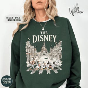 A woman wearing a green sweatshirt with a graphic of Disney characters crossing the street.