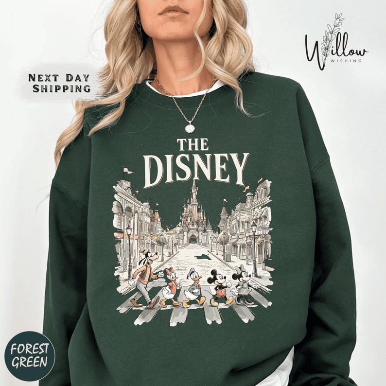 A woman wearing a green sweatshirt with a graphic of Disney characters crossing the street.
